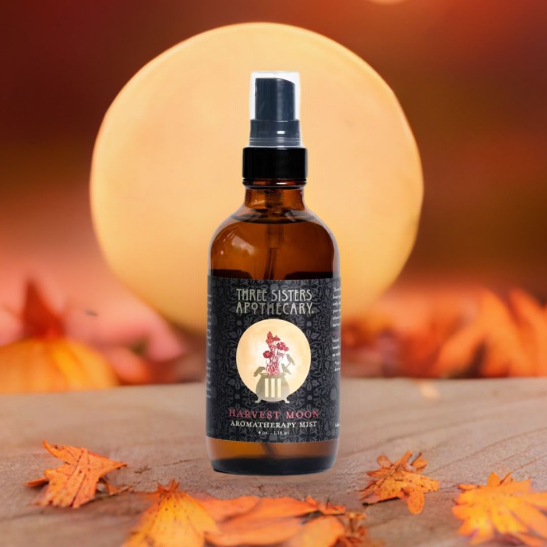 A bottle of Harvest moon aromatherapy spray mist on a wooden surface with autumn leaves scattered around, indicating a fall theme.