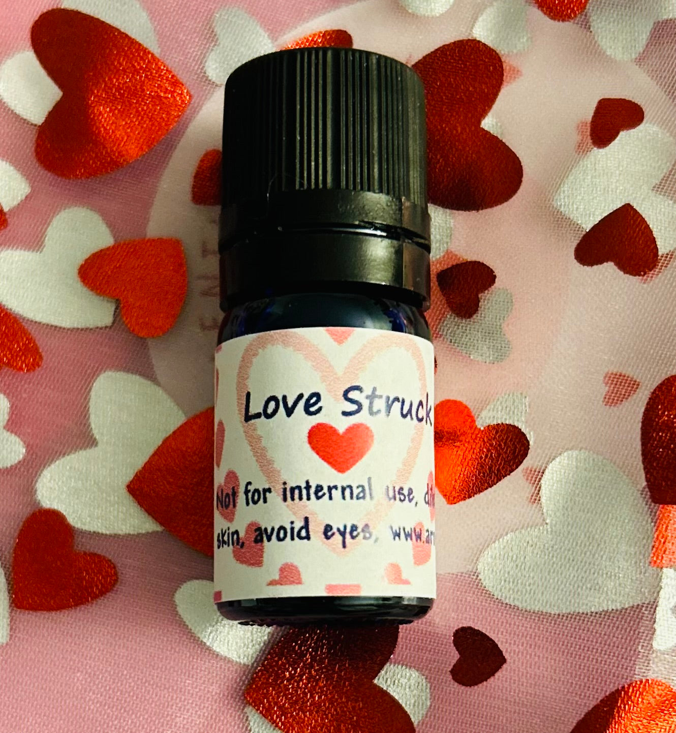 Small bottle of essential oil blend labeled 'Love Struck' on a pink background with heart shapes